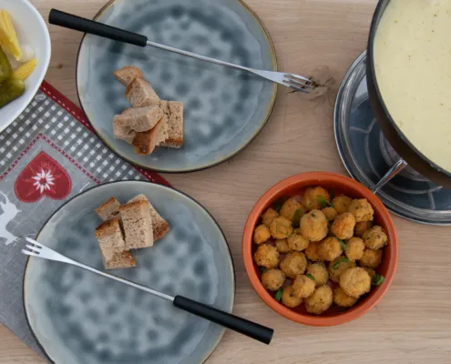 Käsefondue im Caquelon mit Brotwürfeln und Beilagen, von oben fotografiert